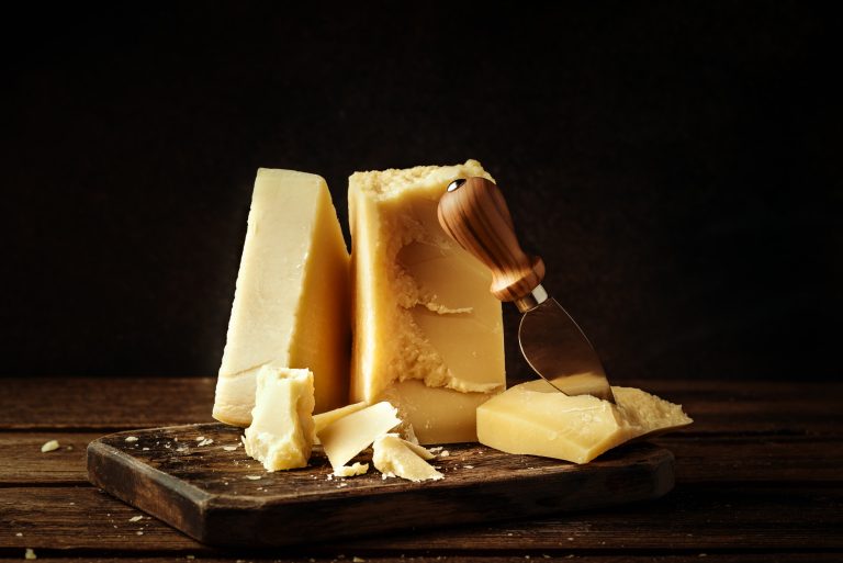Parmesan cheese on wooden board. Pieces of cheese parmesan on wooden table and cheese knife. Vintage view