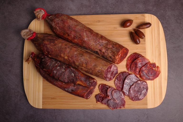 Iberico sausage, Iberico chorizo and Iberico loin on cutting board and dark gray table, garnished with acorns